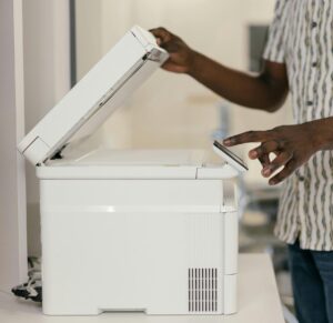 Person operating photocopier in modern office setting, engaging with technology.
